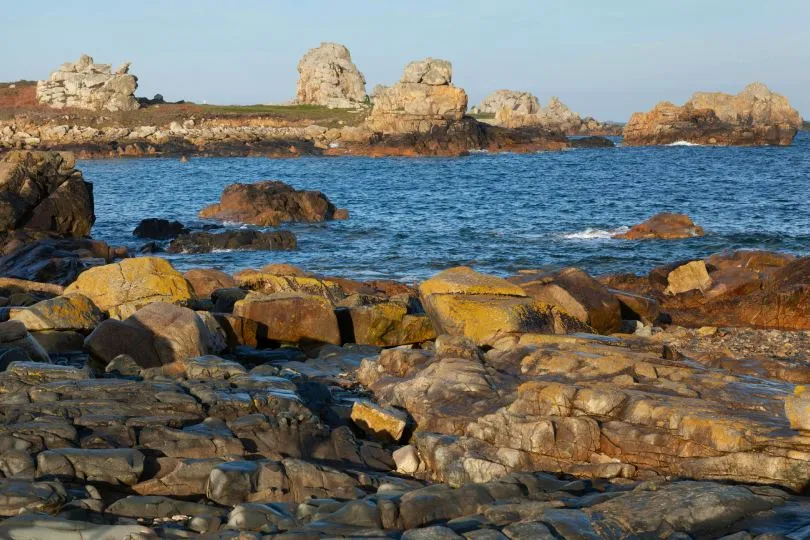 Felsige Küstenlandschaft bei Plougrescant mit zerklüfteten Granitfelsen im Meer und im Vordergrund, unter klarem Himmel.