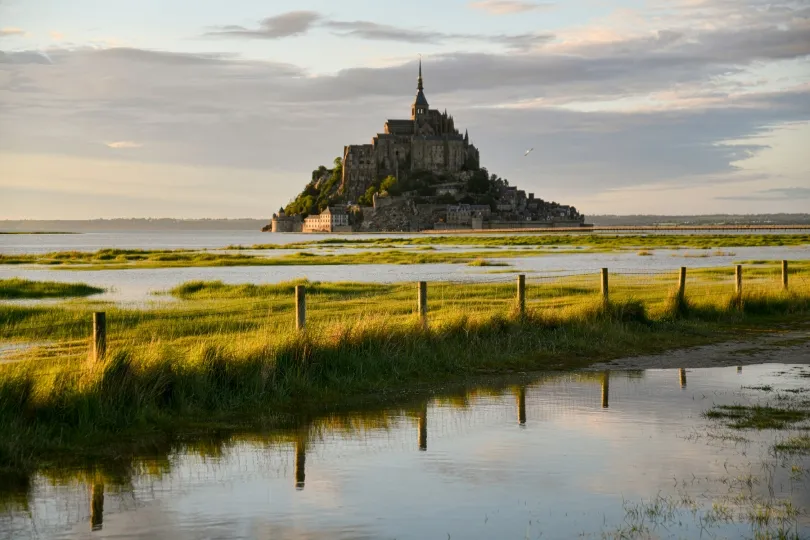 Mont-Saint-Michel in der Normandie mit Abtei auf einer Insel, umgeben von Wasser und grünen Wiesen bei warmem Abendlicht
