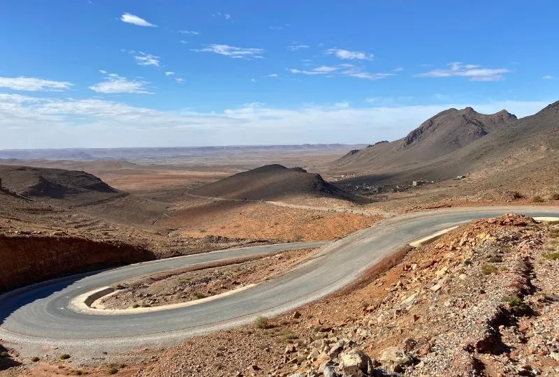 Sehr kurvige, asphaltierte Straße führt durch eine karge, rot-bräunlichen Berglandschaft in Marokko.