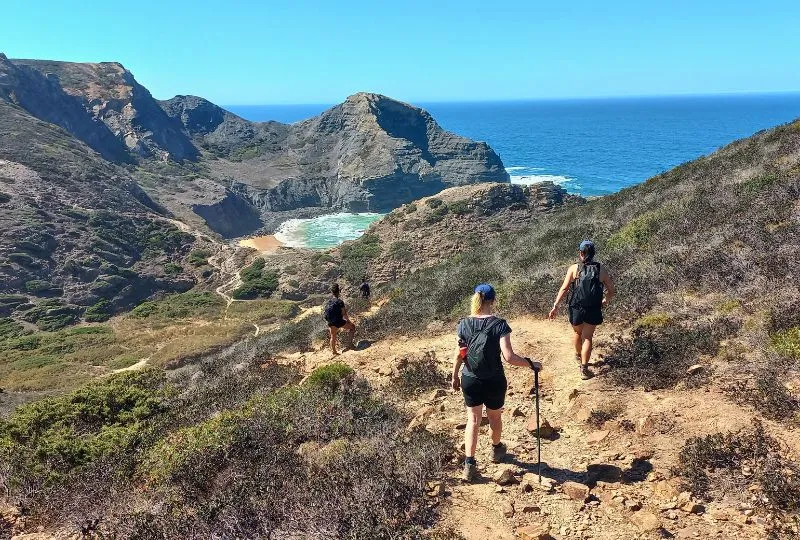Wanderer auf dem Fischerweg im Portugal steigen in ein grünes Tag ab. Vor ihnen liegt der Ozean.