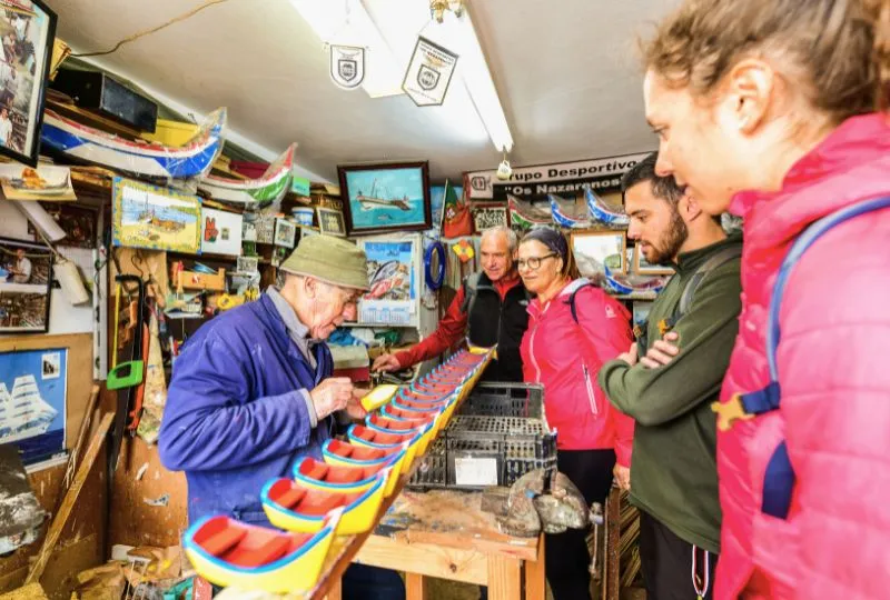 Portugiesischer Kunsthandwerker präsentiert einigen Touristen seine Bootfiguren aus Holz. 