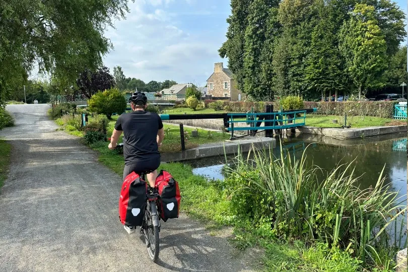 **Alt-Text:** Radfahrer mit Gepäcktaschen auf einem Radweg entlang eines Kanals in der Bretagne.
