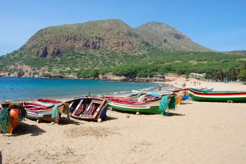Bunte Fischerboot liegen am Strand der Insel Santiago, Kapverden. Im Hintergrund sind grüne Berge zu sehen.