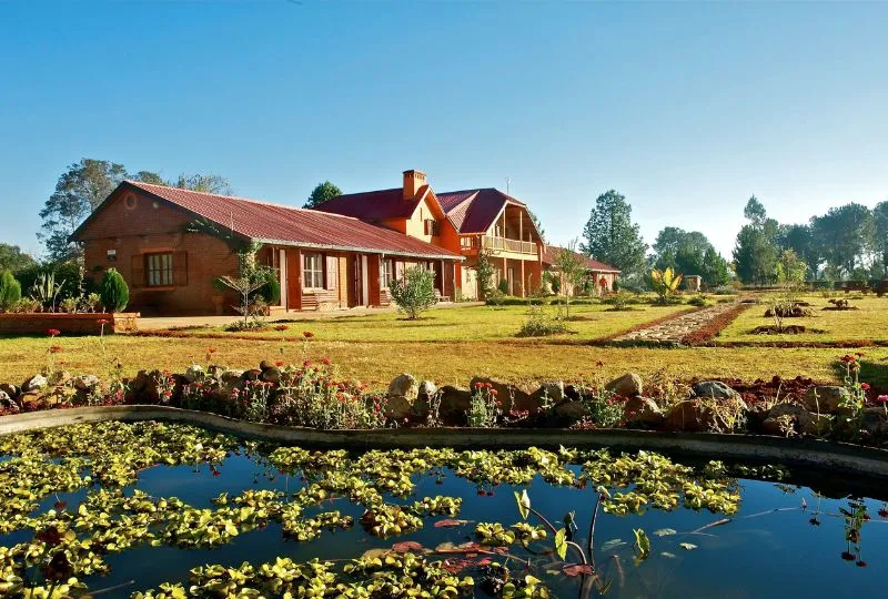 Die Residence Madalief in Madagaskar mit seinem rötlichen Anstrich auf dem grünen Gelände mit einem kleinen Teich im Vordergrund.