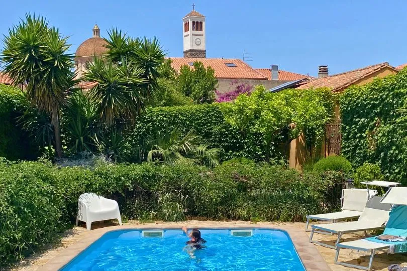 Hotelpool in Sardinien mit einigen Liegen, umgeben von grüner Vegetation.