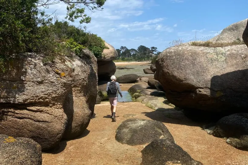 Wanderer auf einem Küstenweg in der Bretagne mit Blick auf Felsen, Meer und blauen Himmel.