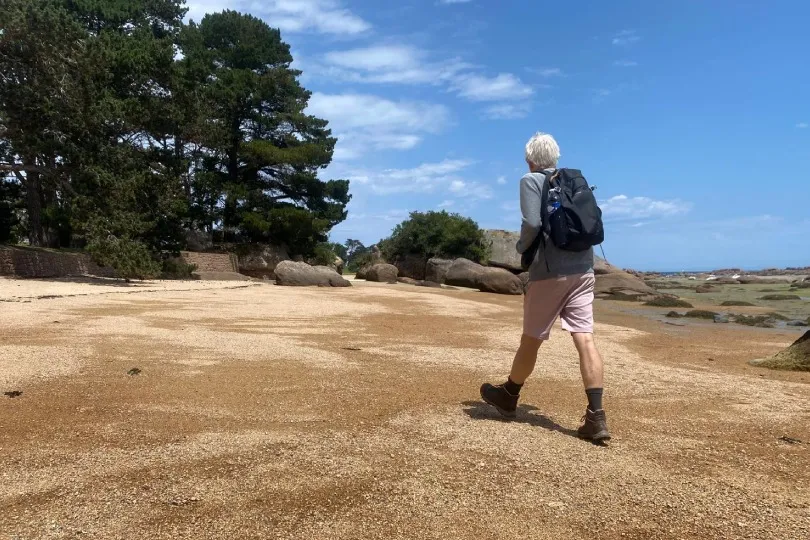Wanderer auf einem Küstenweg in der Bretagne mit Blick auf Felsen, Meer und blauen Himmel.