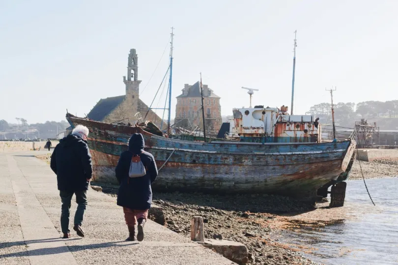 Altes steinernes Rettungsbootshaus am Wasser in Barfleur, Normandie. Eine betonierte Slipanlage mit Schienen führt direkt vom Meer zu einem großen grünen Tor.
