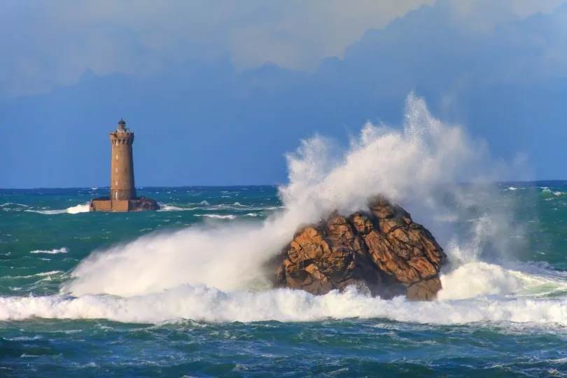 Golven klappen op een rots voor de Le Four vuurtoren in Bretagne, Frankrijk.