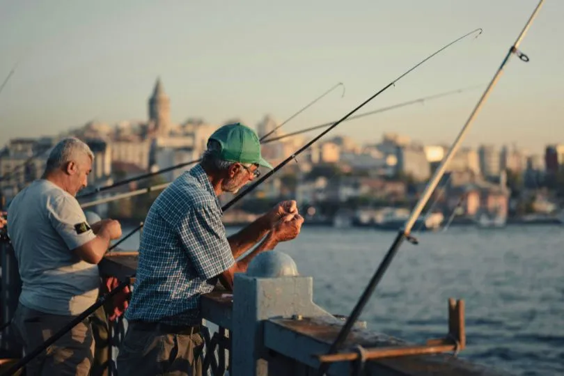 Zwei Angler stehen am Hafen einer Stadt und bereiten ihre Köder vor.