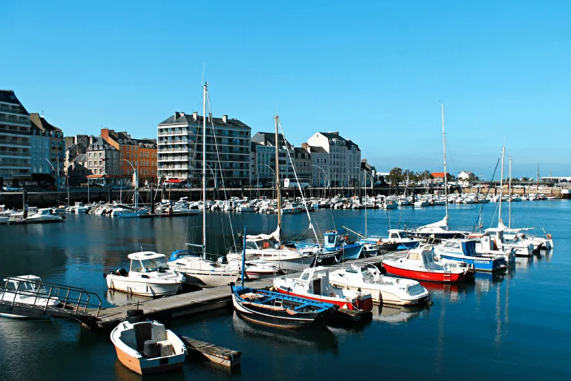 Der Hafen Cherbourg mit kleinen Segelschiffen und der Stadt im Hintergrund.
