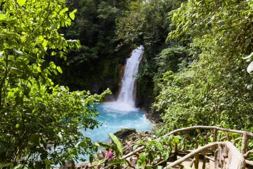 Ein Wasserfall fällt in ein türkises Becken des Río Celeste in Costa Rica, umgeben von grüner Vegetation.