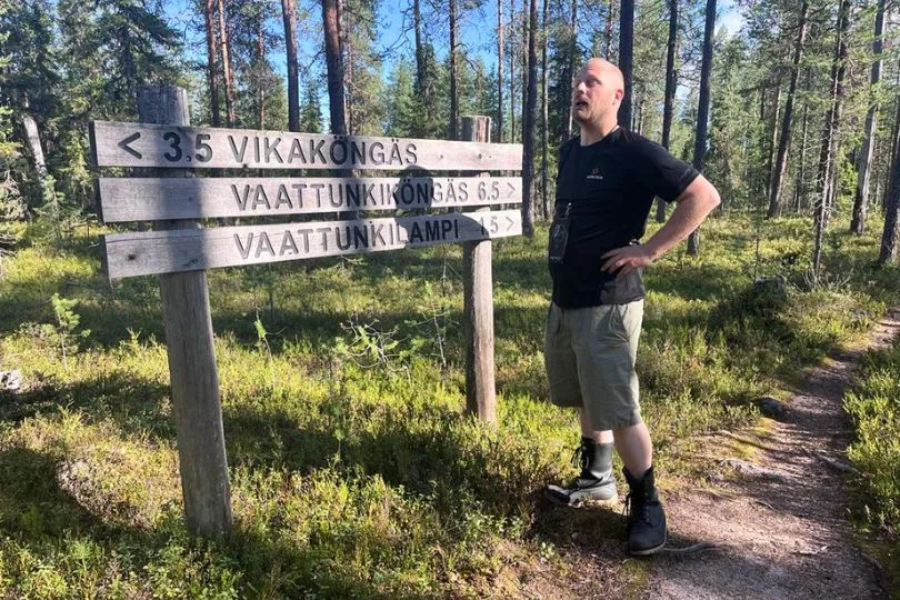Mann steht vor einem Wegweiser in Finnland mit sehr langen Wörtern und schaut verwirrt drein.