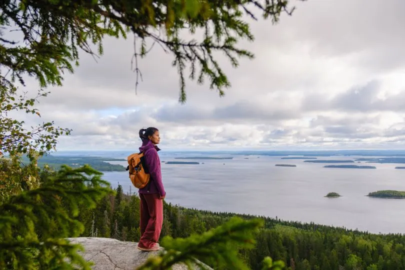 Wanderin steht auf einem Aussichtpunkt über einer Landschaft von Wasser und Inseln im Koli Nationalpark, Finnland.