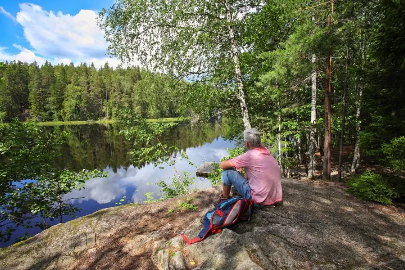 Frau sitzt auf einem Felsen am See im Nuuksio Nationalpark, Finnland.
