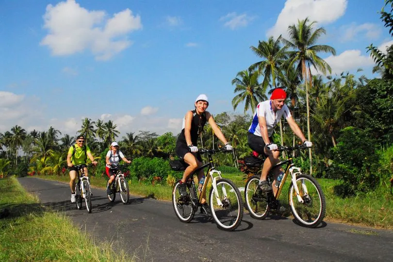 Touristen fahren auf Fahrrädern über eine Landstraße in Indonesien.