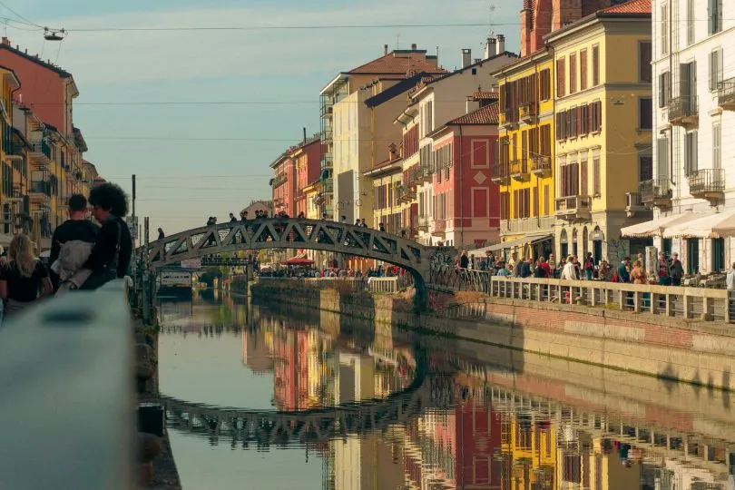 Bunte Häuser und eine kleine Stahlbrücke spiegeln sich im ruhigen Wasser eines Kanals in Mailand, Italien.