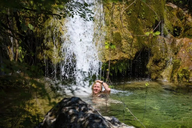 Frau steht unter einem kleinen Wasserfall in einem natürlichen Wasserbecken in Montenegro.