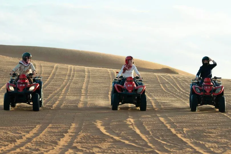 Drei Touristen fahren mit Quads durch die Sandwüste.