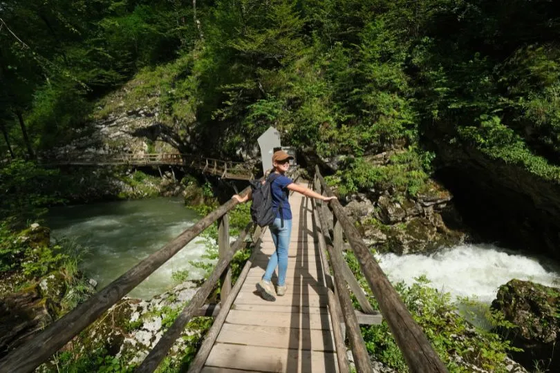 Mädchen steht auf einer Holzbrücke über einem Fluss im Wald in Slowenien und dreht sich zur Kamera um.