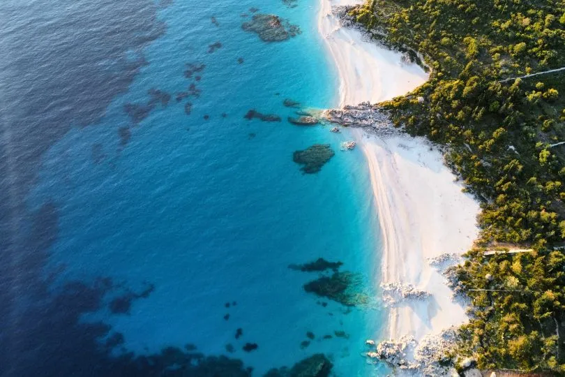 Vogelperspektive über einen weißen Sandstrand und das Meer direkt neben dem Wald, in der Nähe von Dhermi, Albanien.