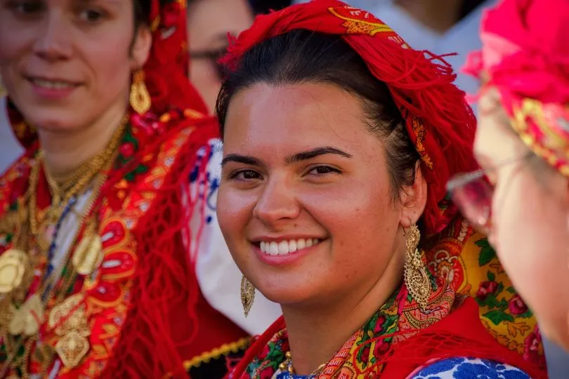 Albanerin in roter Tracht mit goldenen Ohrringen lacht in die Kamera.