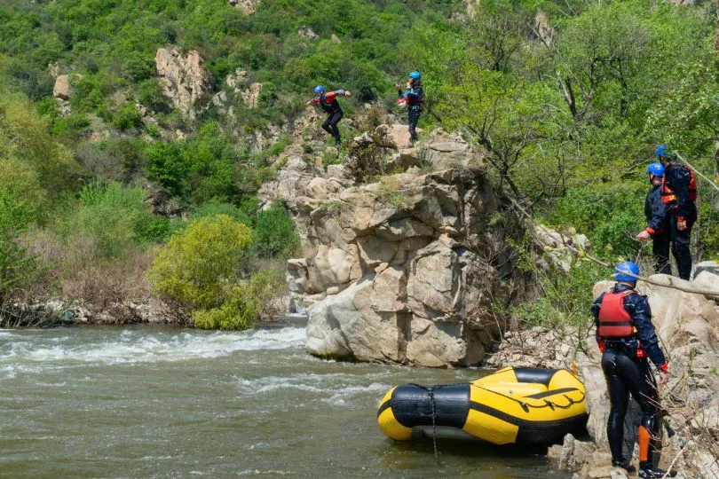 Reisende beim Raften am Struma Fluss in Bulgarien klettern gerade einen Felsen runter zum Wasser.
