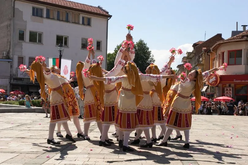 Frauen in Tracht in Bulgarien führen einen Tanz mit Rosen in der Hand auf.