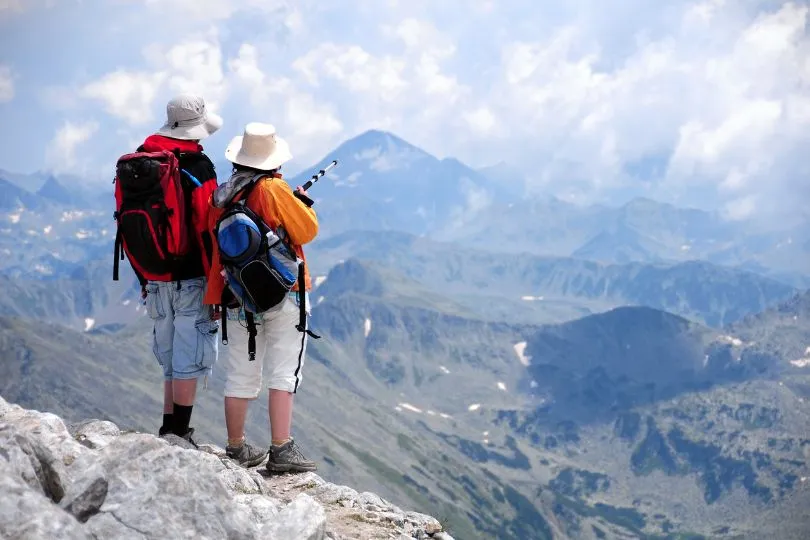 Zwei Wanderer stehen auf dem Vihren Gipfel in Bulgarien und schauen auf die Lanschaft hinab.