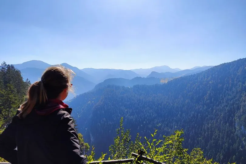 Reisende steht auf einem Aussichtspunkt in Bulgarien und schaut auf ein bläulich leuchtendes Bergpanorama.