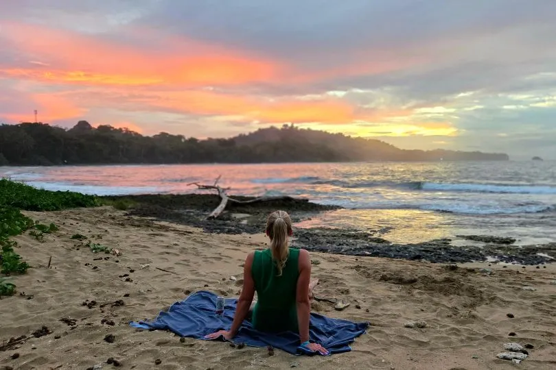 Frau sitzt in Costa Rica am Strand und schaut den Sonnenuntergang.