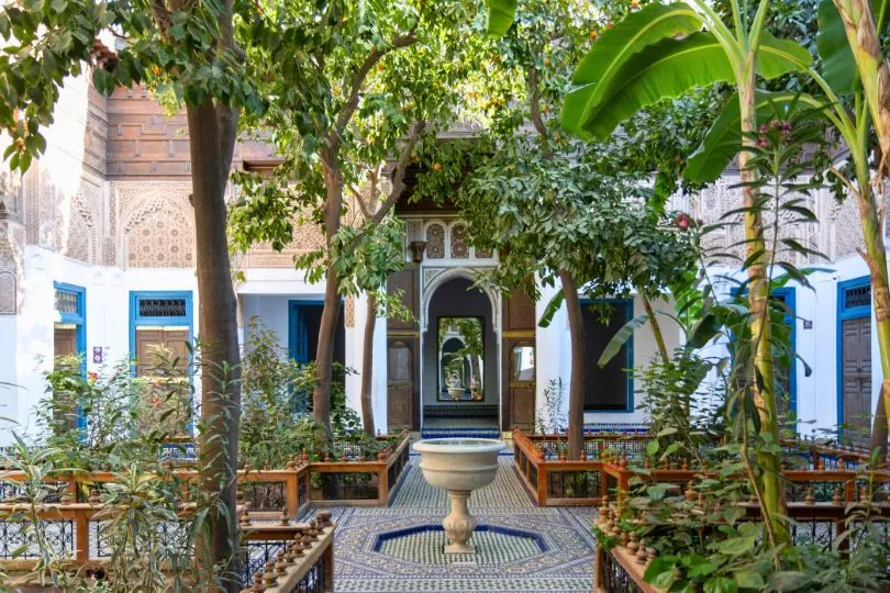 Der Innenhof des Bahia Palastes in Marokko mit Brunnen, verschiedenen Bäumen und bunten Kacheln auf dem Boden.