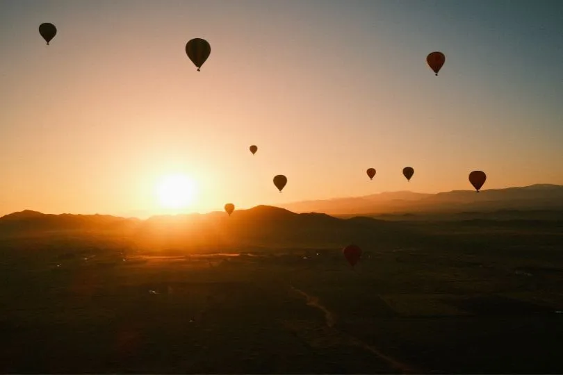Heißtluftballons fliegen bei Sonnenuntergang über die Wüste Marokkos.