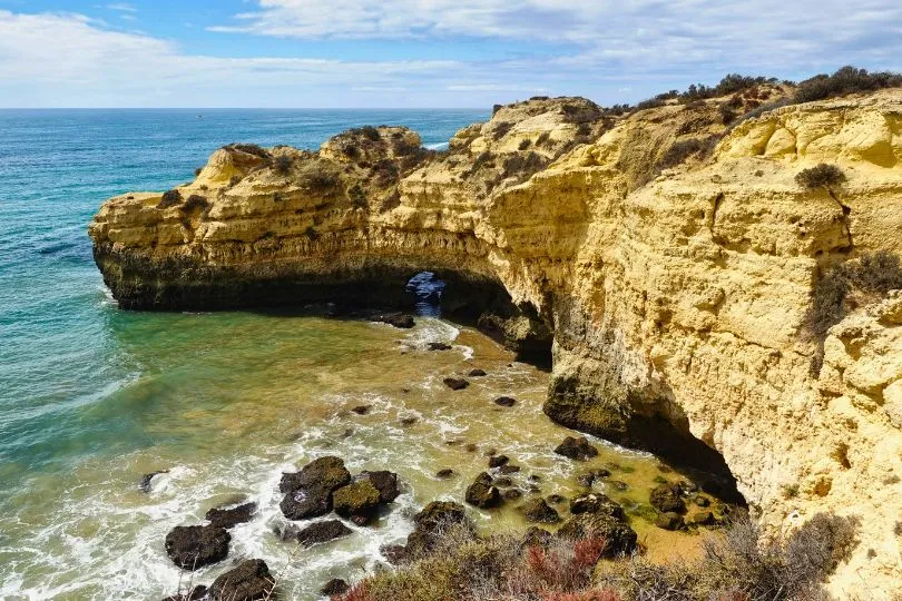 Eine felsige Klippe an einer natürlichen Bucht in Portugal ragt ins Wasser.