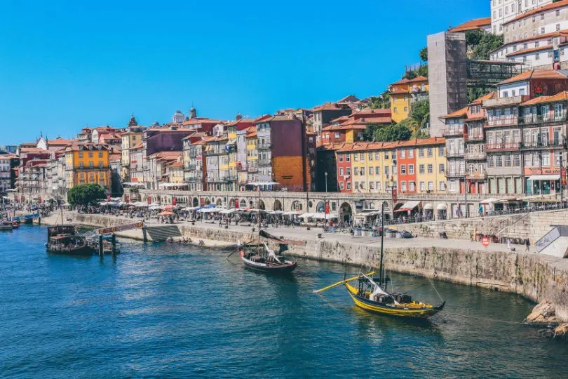 Kleine Fischerboote stehen vor der Promenade und den bunten Häusern in Porto.