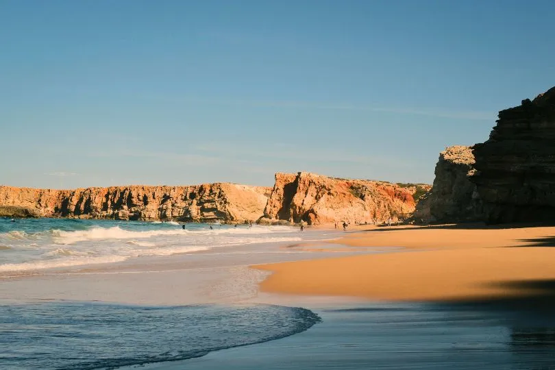 Einsamer Sandstrand im Abendlicht vor beeindruckenden Felsklippen in der Algarve, Portugal.