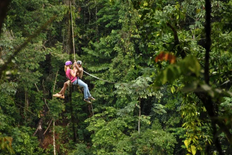 Zwei Mädchen hängen an einer Zipline mitten im dichten Dschungel Surinames.