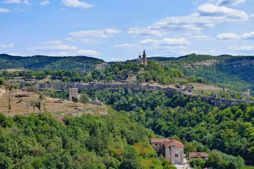 Aussicht auf eine bergige Landschaft voller Bäume in Bulgarien. Dazwischen stehen einige Gebäude und eine Mauer.