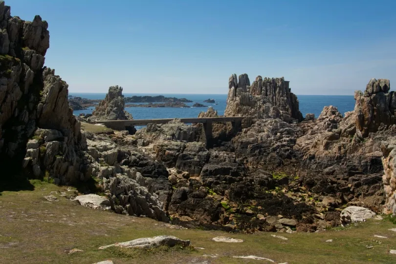 Schroffe Felsküste auf der Île d’Ouessant in der Bretagne mit einer schmalen Brücke zwischen markanten Felsformationen und dem Atlantik im Hintergrund.