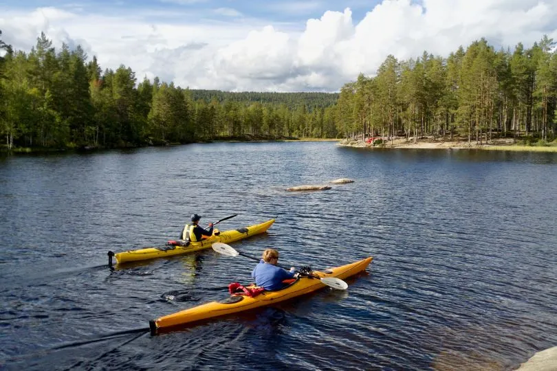 Zwei Personen paddeln mit dem Kajak durch das tiefblaue Wasser des Stockholmer Schärengartens.