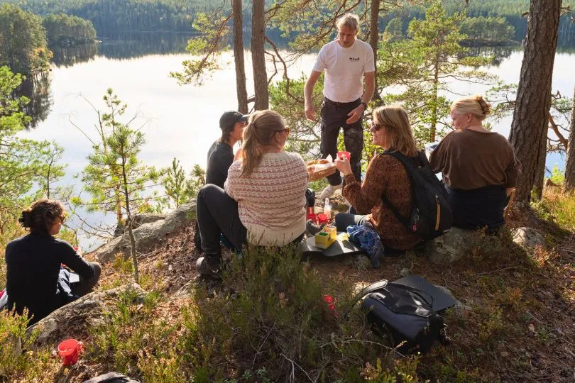 Eine Gruppe Reisender sitzt an einem See in Schweden und genießt eine Mittagspause. 