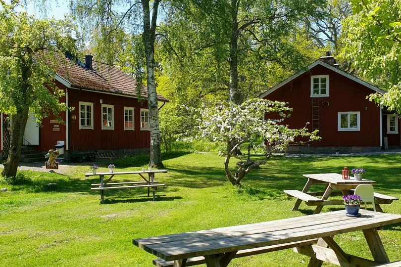 Rastplatz mit Bänken und Tischen vor roten Holzhäusern in Schweden.