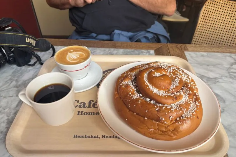 Eine schwedische Fika mit Kaffee und einer großen Zimtschnecke steht auf einem Tablett.