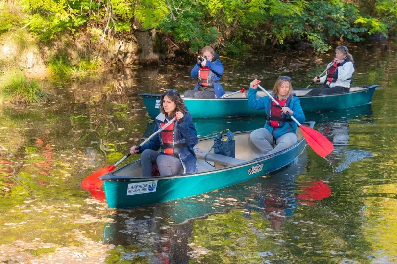 Vier Frauen sitzen jeweils zu zweit auf einem Kanu und paddeln durch ein Gewässer in Schweden.