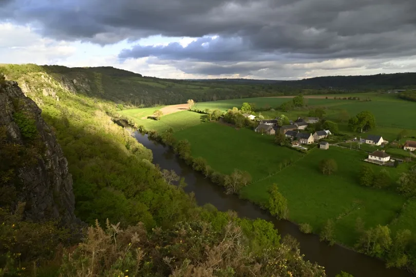 Blick über die Vallée du Don bei Guémené-Penfao mit dem gewundenen Fluss Don, grünen Feldern, bewaldeten Hängen und einem kleinen Dorf unter dramatischem Wolkenhimmel.