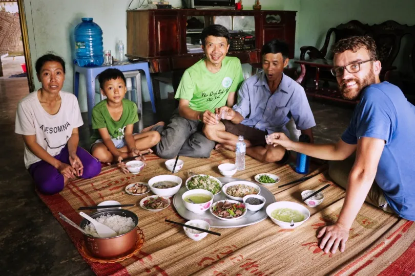 Eine Familie und zwei Gäste sitzen gemeinsam auf dem Boden und essen.