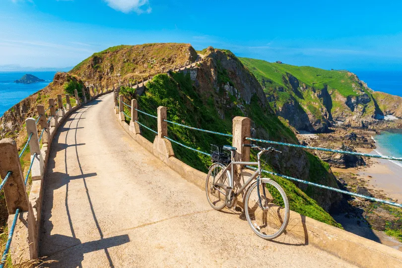 Fahrrad an einem schmalen Küstenweg auf Sark, umgeben von grünen Steilklippen und mit Blick auf das Meer.