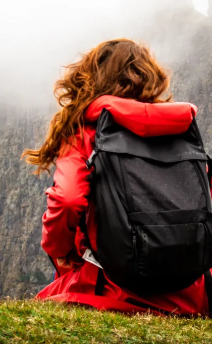 Eine Frau sitzt vor einem Berg mit ihrem Rucksack