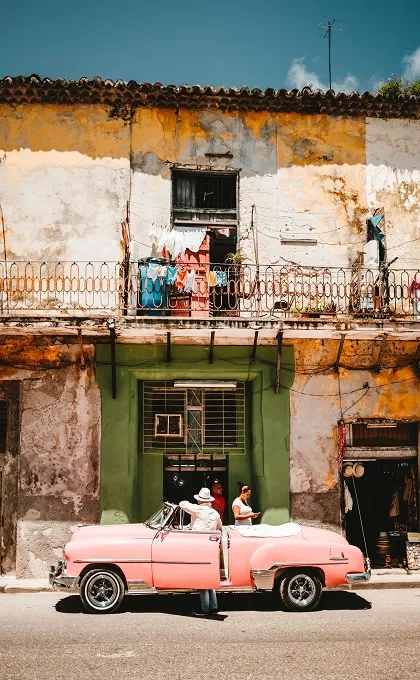 Pinker Oldtimer vor einem bunten Haus in Havanna