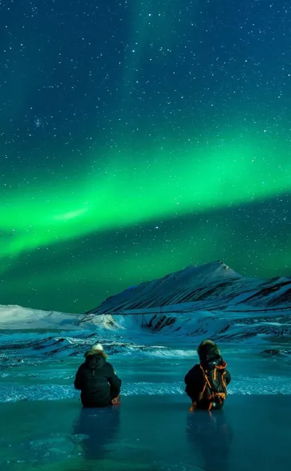 zwei Perosnen sitzen und schauen sich die Nordlichter an.